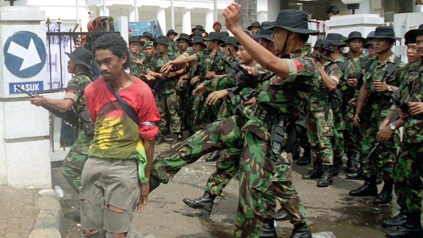 A soldier kicks a student in the backside in front of a line of soldiers to the gates of the foreign ministry