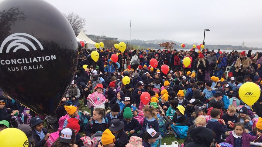 Lots of young children rugged up in warm winter gear holding reconciliation balloons.