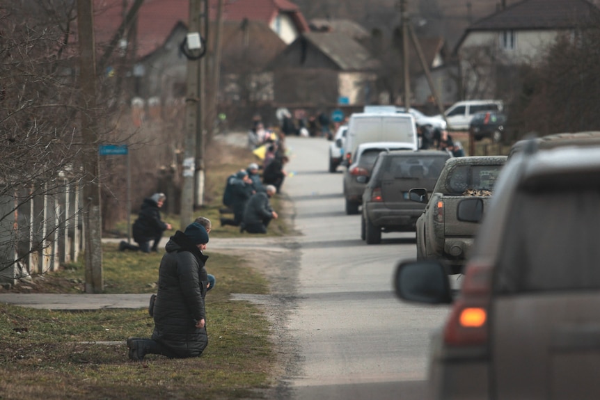 People kneel by the roadside to say the last goodbye to Dmytro "DaVinci" Kotsiubaylo as a convoy of cars drives past.