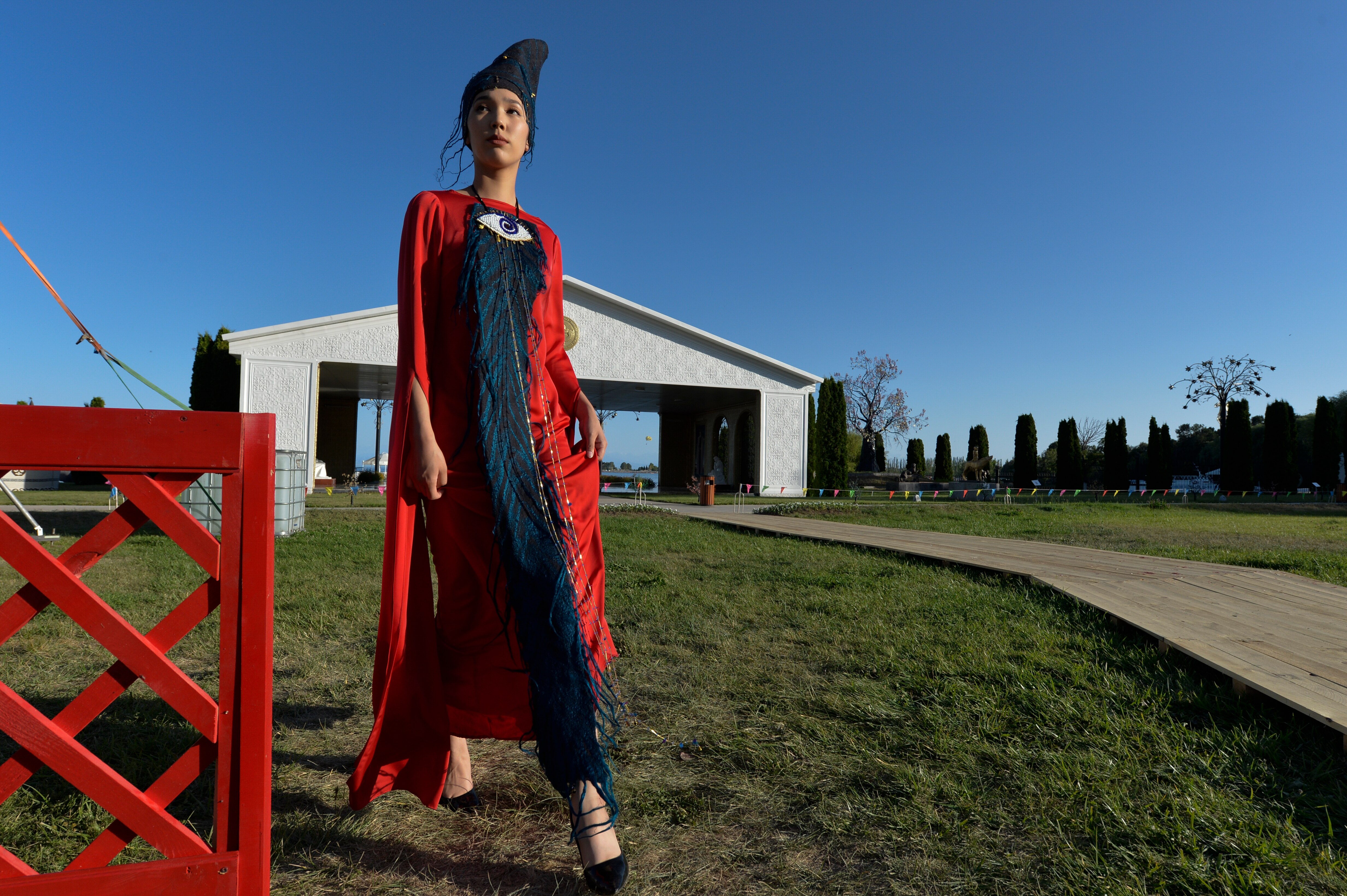 A model dressed in a designer's clothes stands in a field with a shed behind her. 