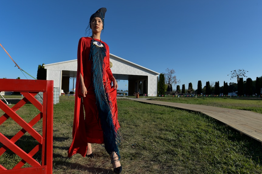 A model in designer clothes stands in a field with a shed behind her. 