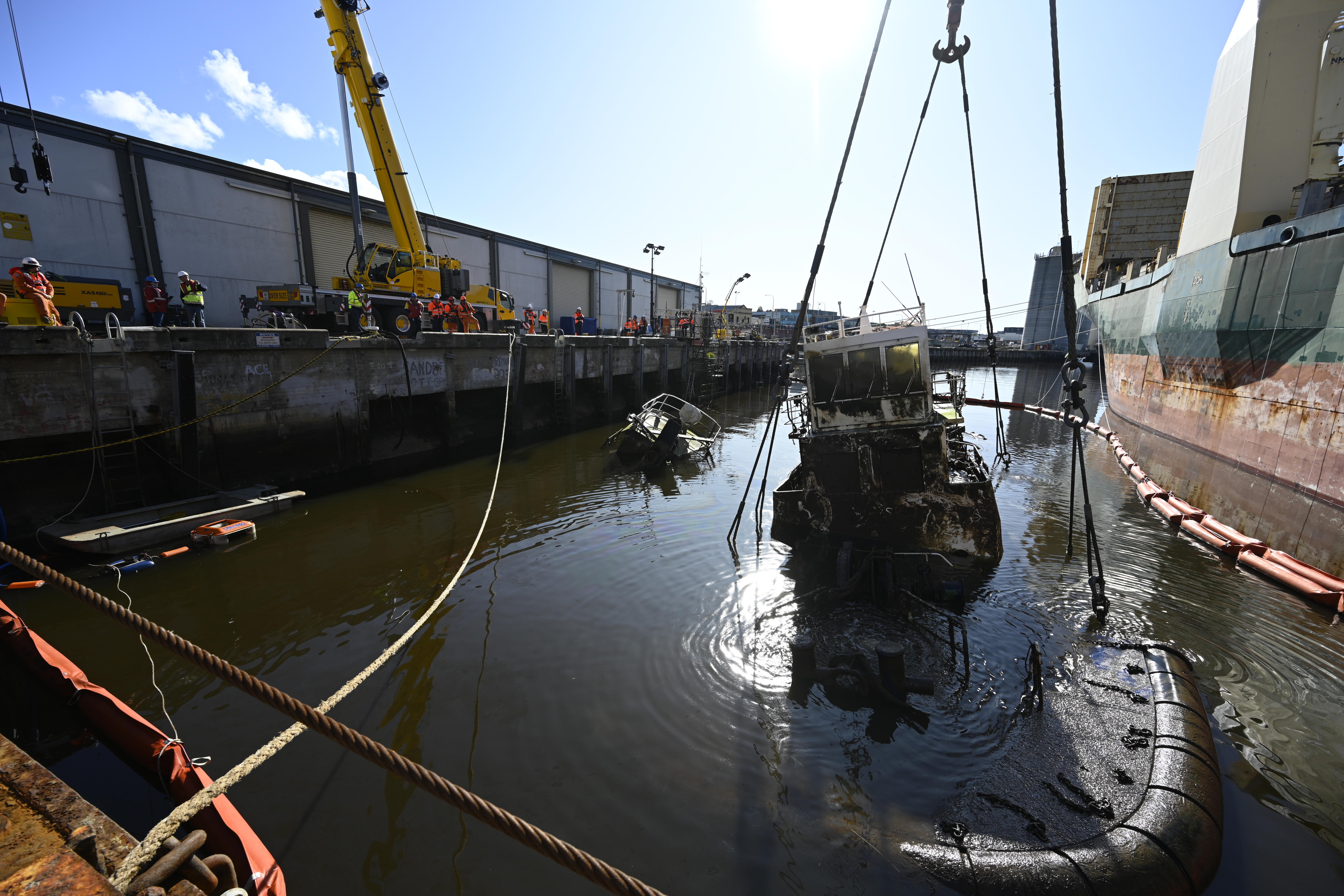 A ship is lifted out of the water by a larger ship at an industrial dock.