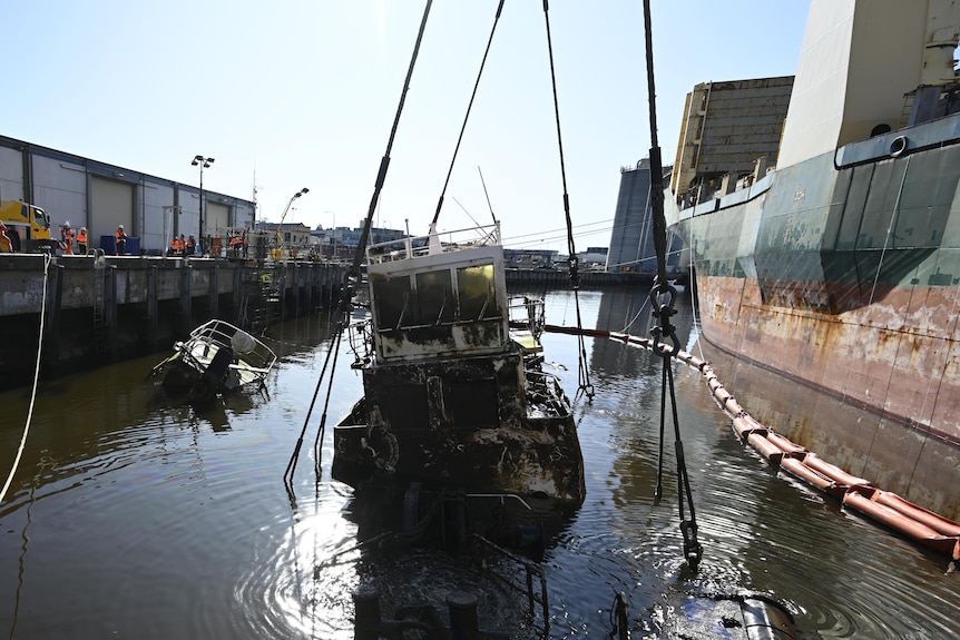 A ship is lifted out of the water by a larger ship at an industrial dock.