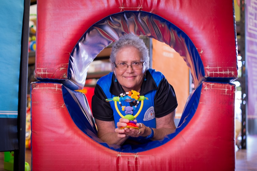 A woman lies in a rubberised toy tunnel holding a plastic baby's toy.