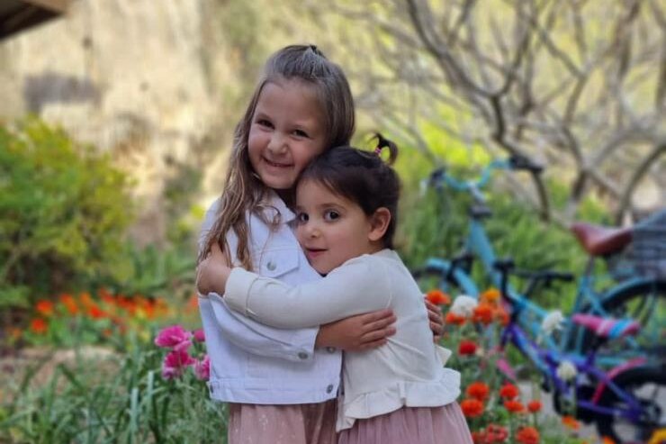 Two young girls hug and smile for the camera while standing in a garden