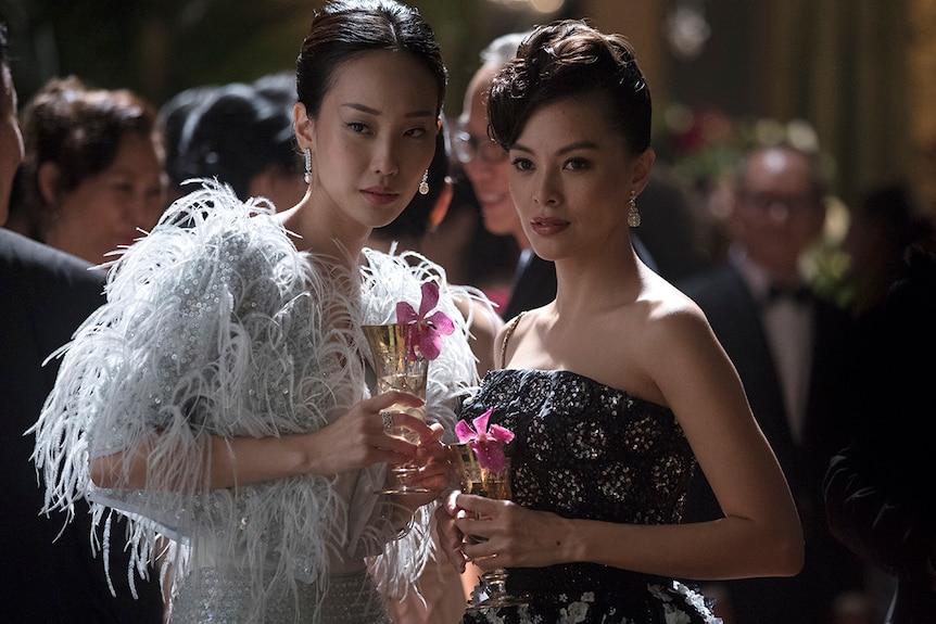 Colour still of actors Constance Lau and Carmen Soo in shiny gowns and holding cocktails in 2018 film Crazy Rich Asians.