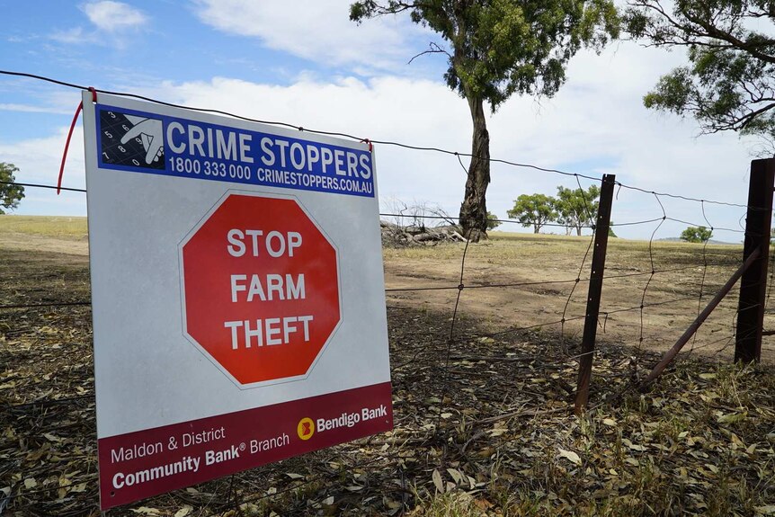 A sign ziptied to a wire fence reads "STOP FARM THEFT"