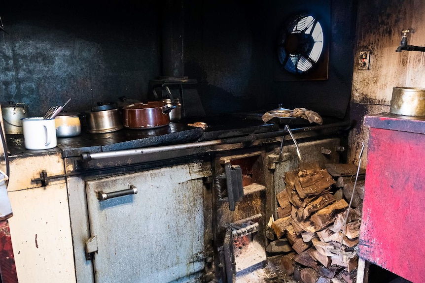 The old aga, covered in soot of years of cooking, with a pile of hard wood to the right ready for burning.