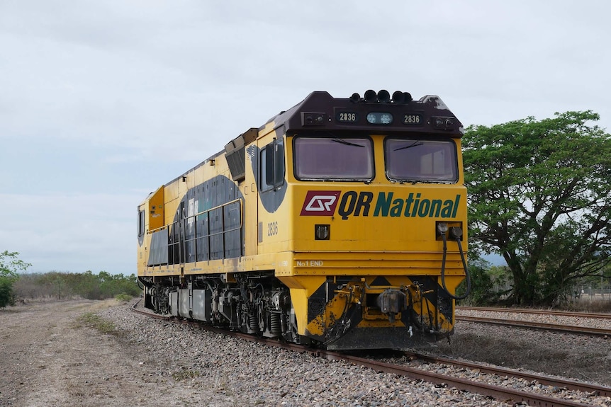 A yellow freight train engine on a track in a rural area.