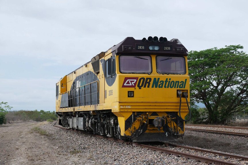 A yellow freight train engine on a track in a rural area.