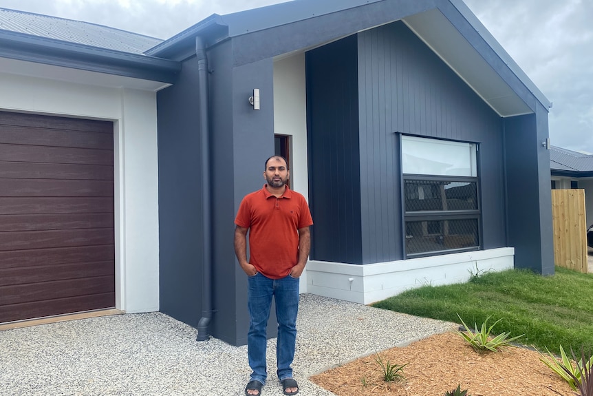 A man standing in front of his brand new home.