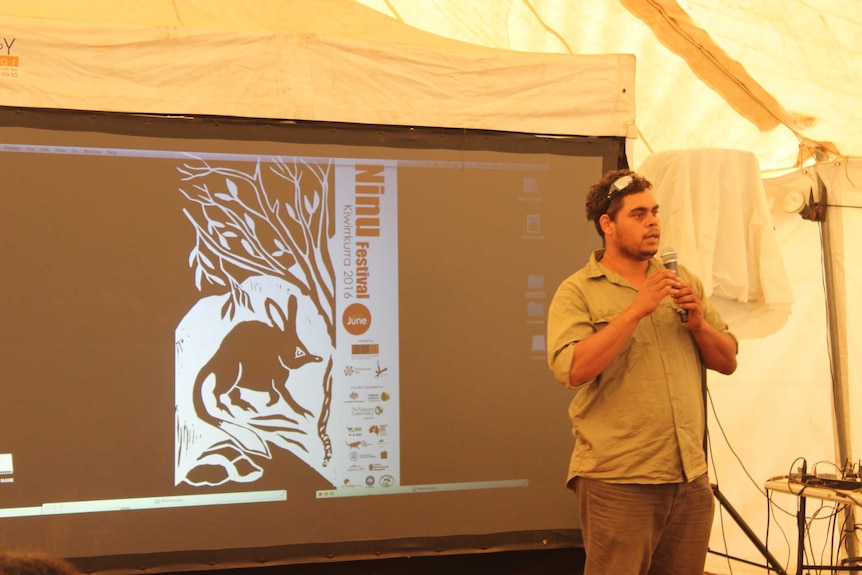 A picture of Patrick Green standing with a microphone next to a projected display.