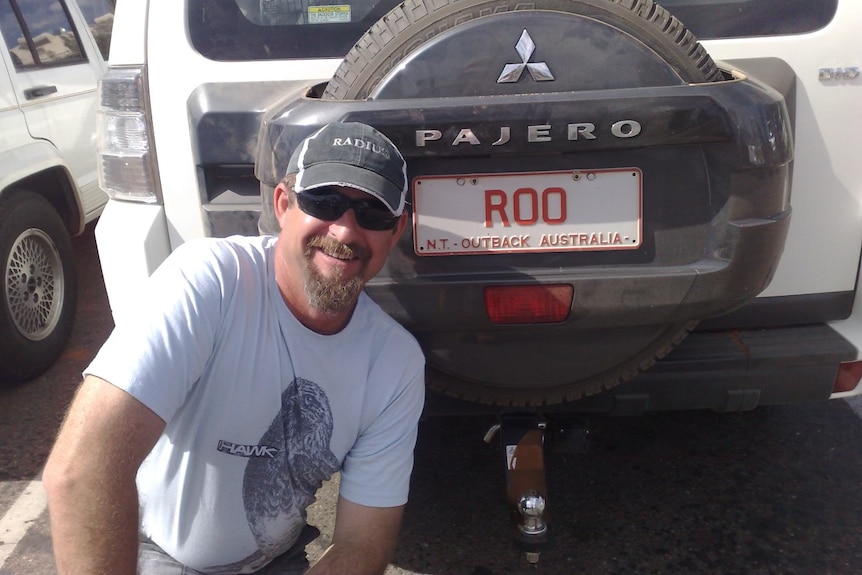 Ray smiling in front of a car licence plate that says 'roo'
