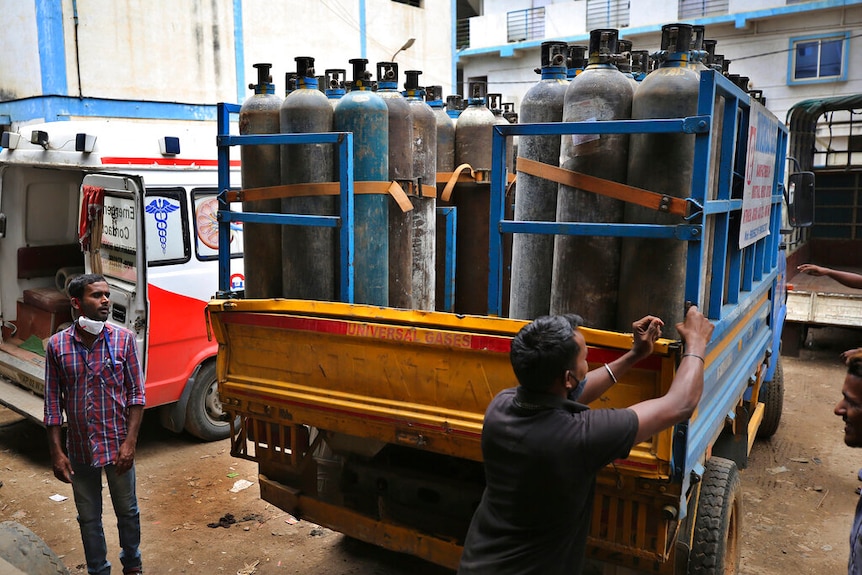 A man closes a trailer of a small truck, which carrries rows of empty oxygen canisters.