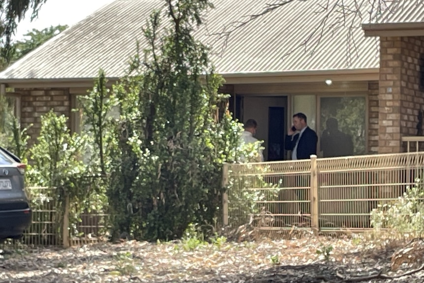 A man in a suit on the phone outside a house.