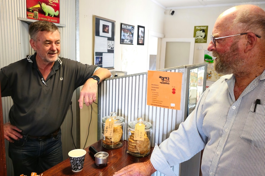 Two men talk over a counter with a coffee