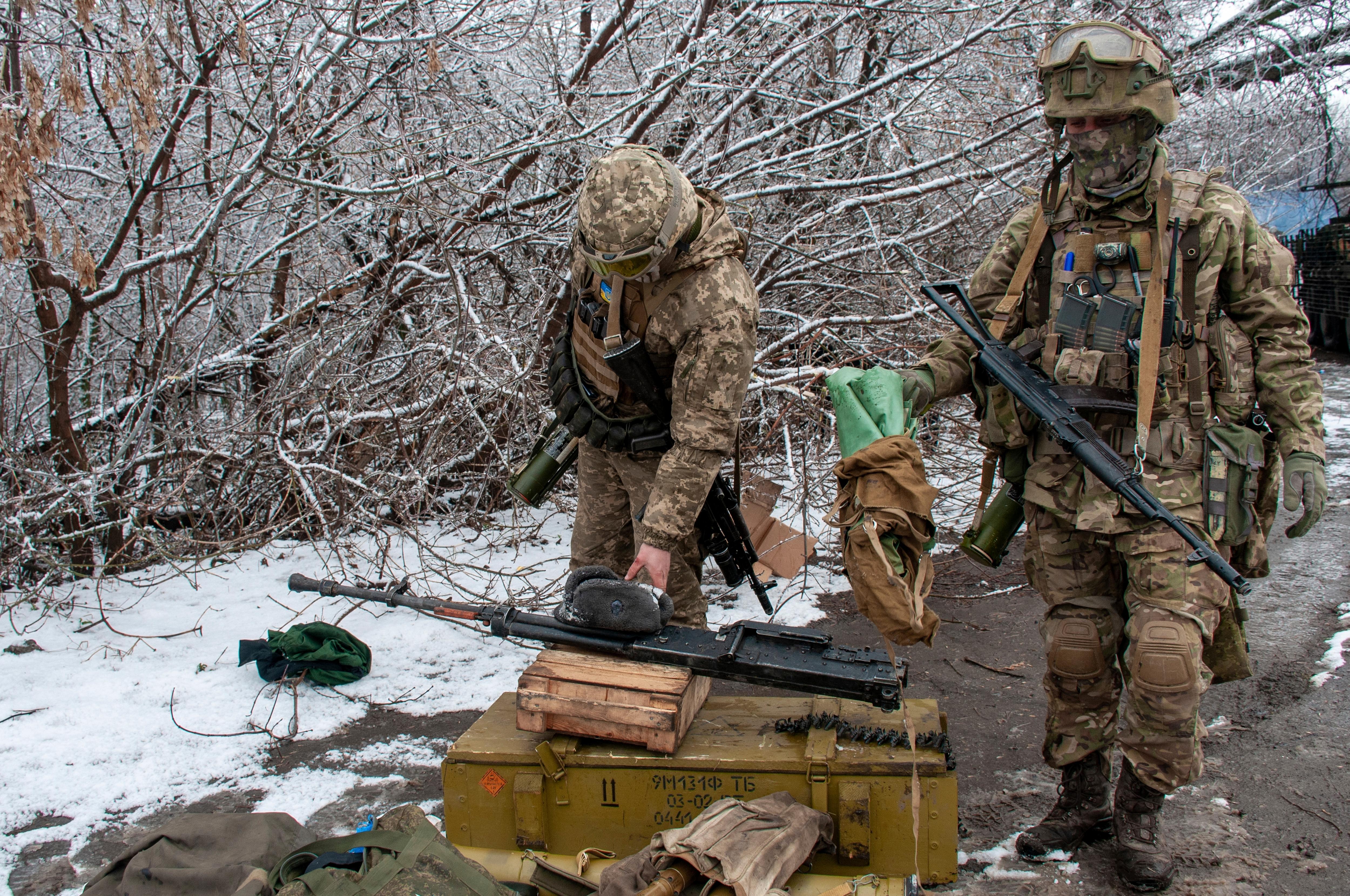 Soldiers in battle gear ready their rifles at a snowy defensive position behind leafless trees.