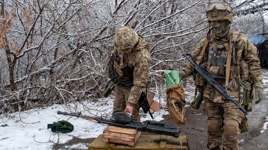 Soldiers in battle gear ready their rifles at a snowy defensive position behind leafless trees.