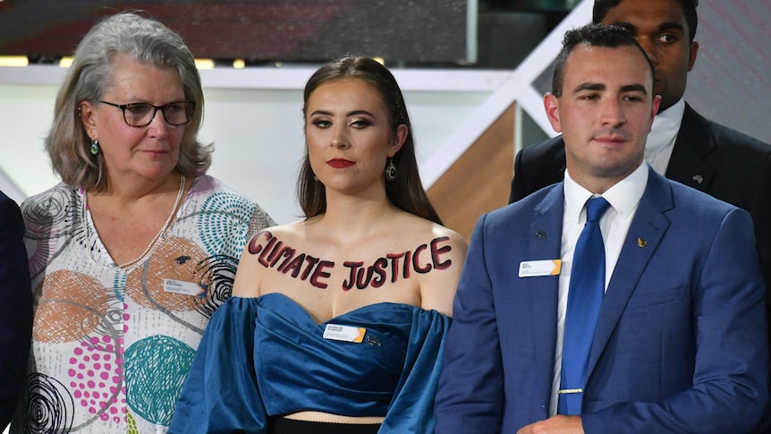 Madeline Diamond stands between a man and woman with Climate Justice written on her upper chest above her blue top