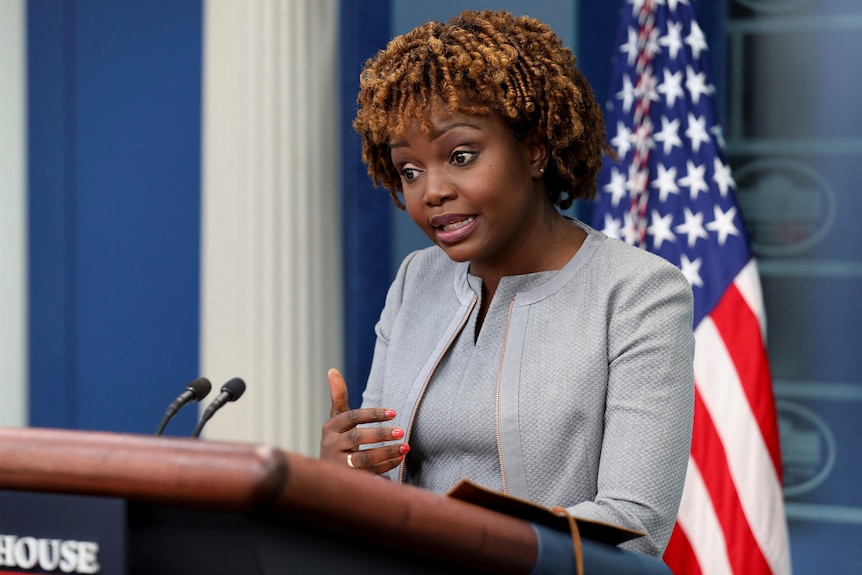 A woman speaks from behind a podium with a US flag behind her