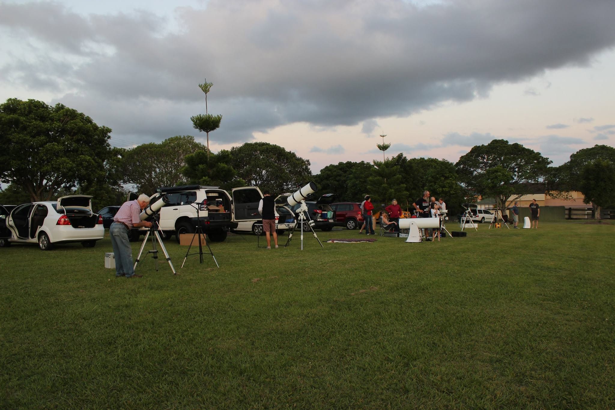 A group of people with telescopes in a grassy field/