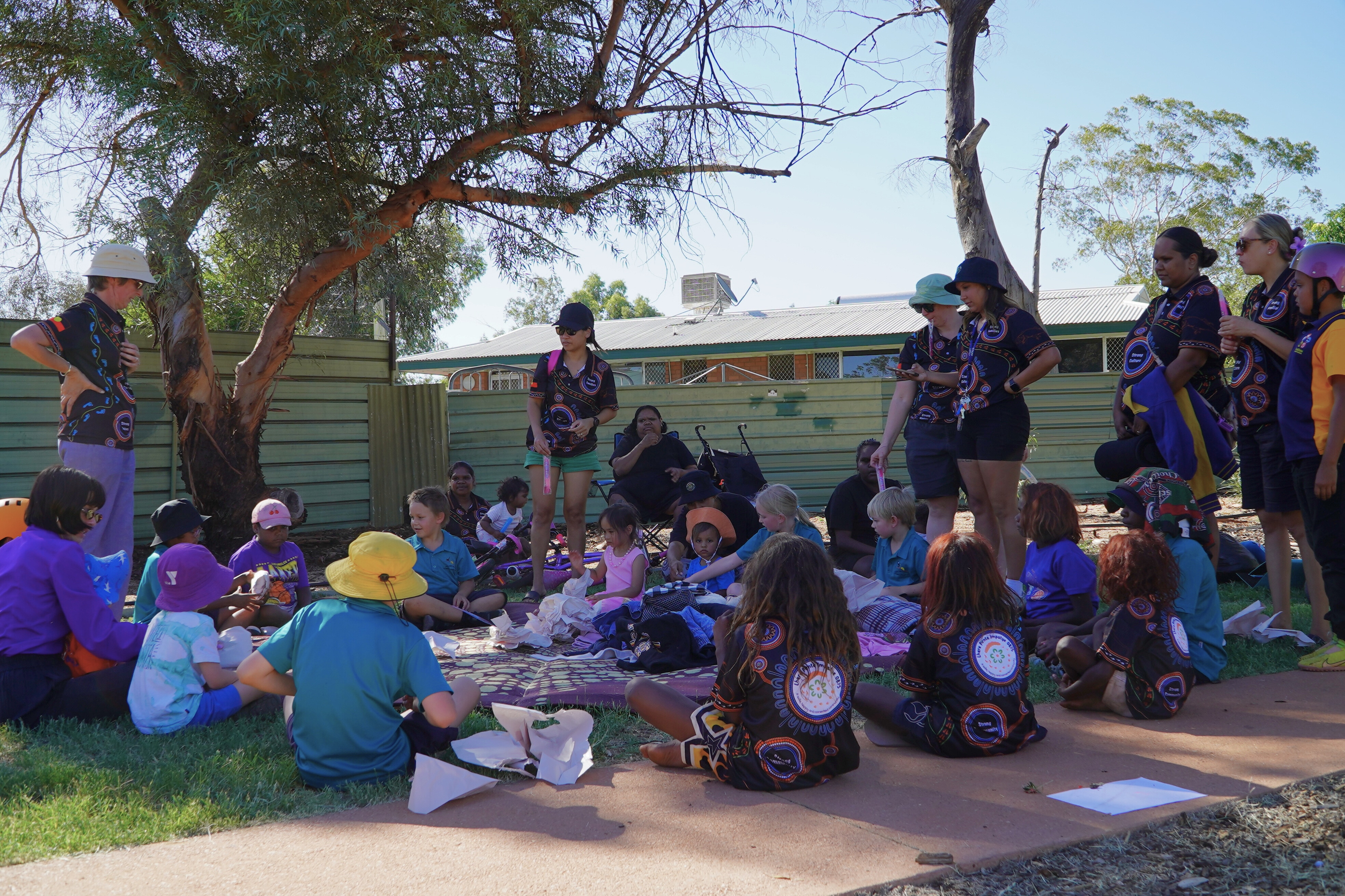 Un grupo de niños se sienta en una zona de césped con sombra en un parque comunitario.