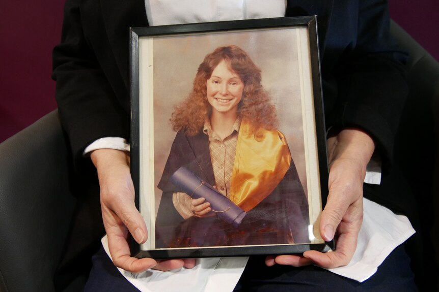 hands holding a graduation picture, showing a girl with curly hair wearing a graduation gown 