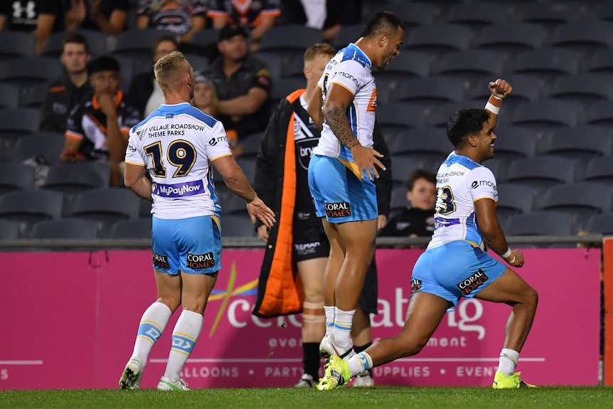 An NRL player runs away with his fist in the air in celebration as his teammates watch.