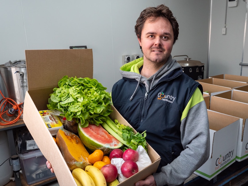 Clint Evans holding a box of fruit and vegetables in a storeroom.