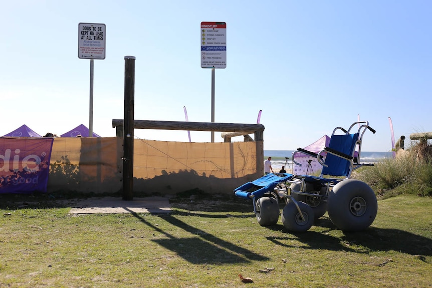 A chunky-wheeled wheelchair sitting empty next to the beach.