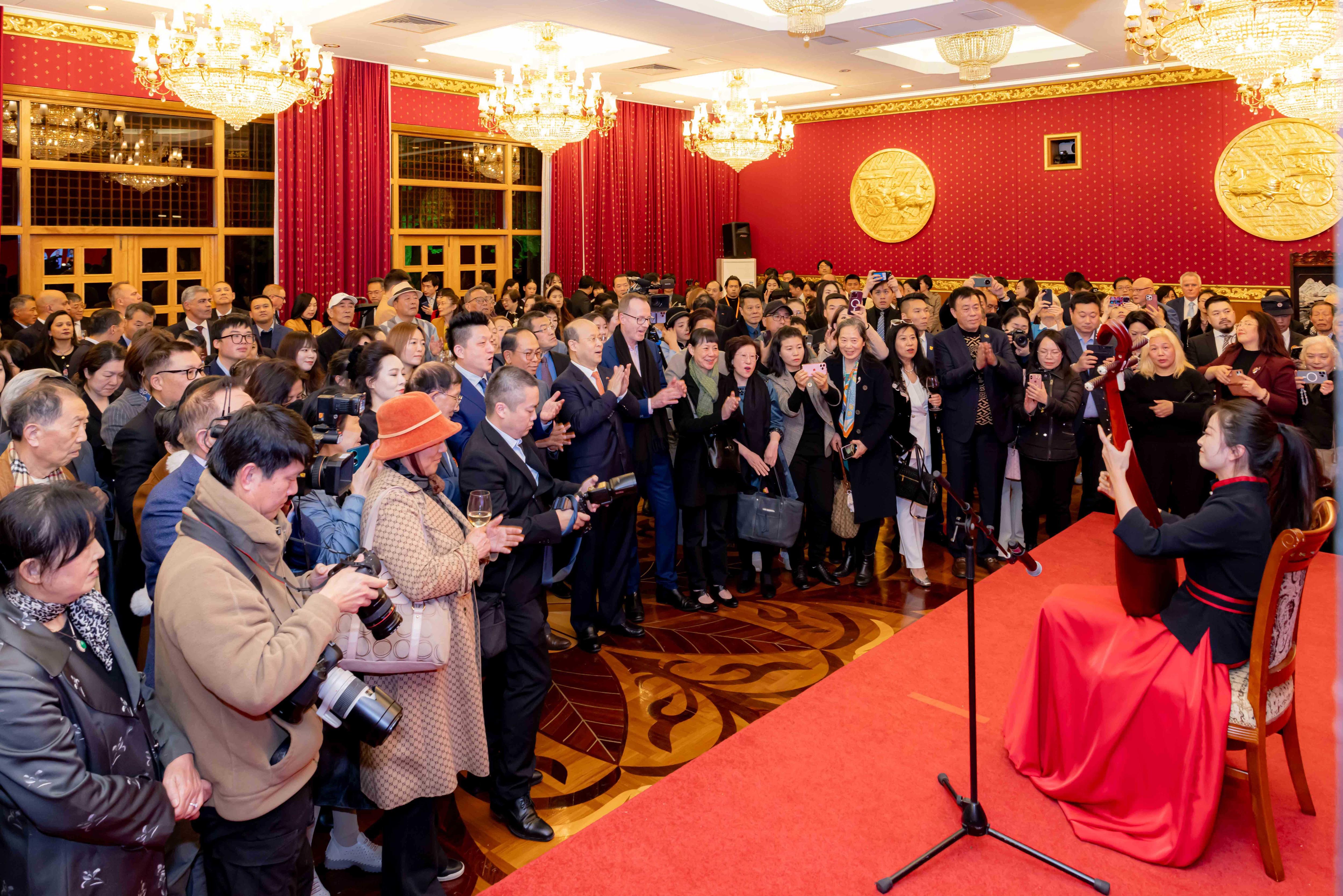 red walled and carpeted room with about 200 people and press watching a woman in red dress play an instrument on red stage.