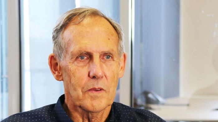 A close up photo of a man's head wearing a dark button up top.