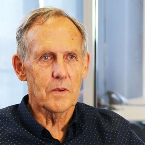 A close up photo of a man's head wearing a dark button up top.