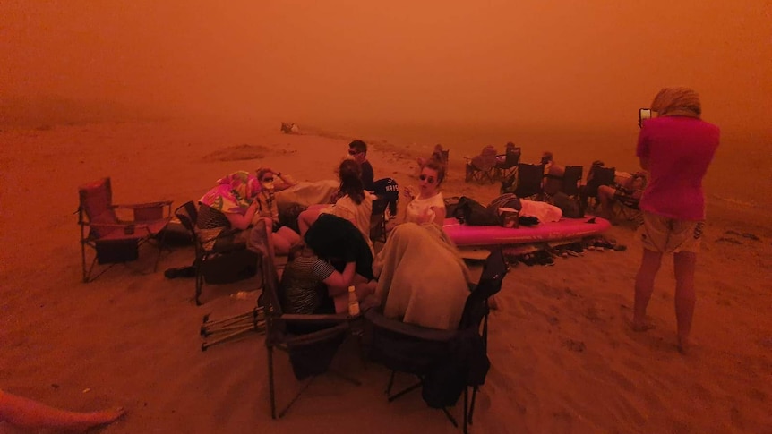 People on a beach against a dark orange haze.