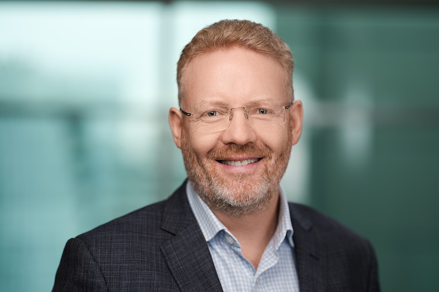 Head shot of a ginger-haired man with a grey flecked beard, wearing glasses and smiling.