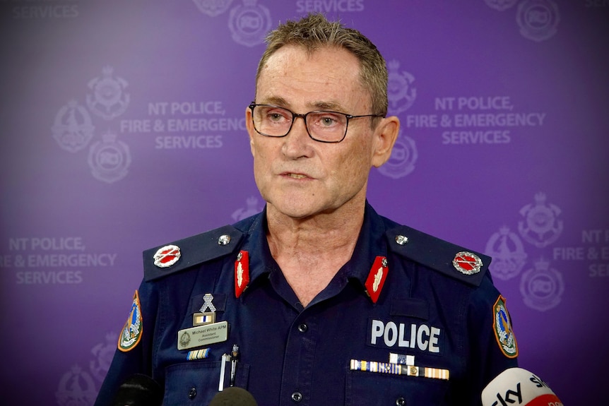 A man wearing dark-rimmed glasses and a police uniform speaks at a press conference