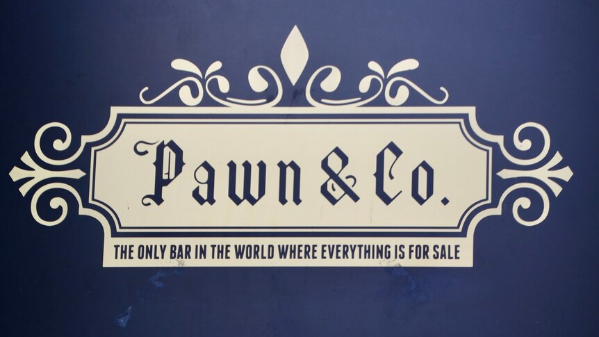 A sign with white writing and blue background that says Pawn & Co: The only bar in the world where everything is for sale.
