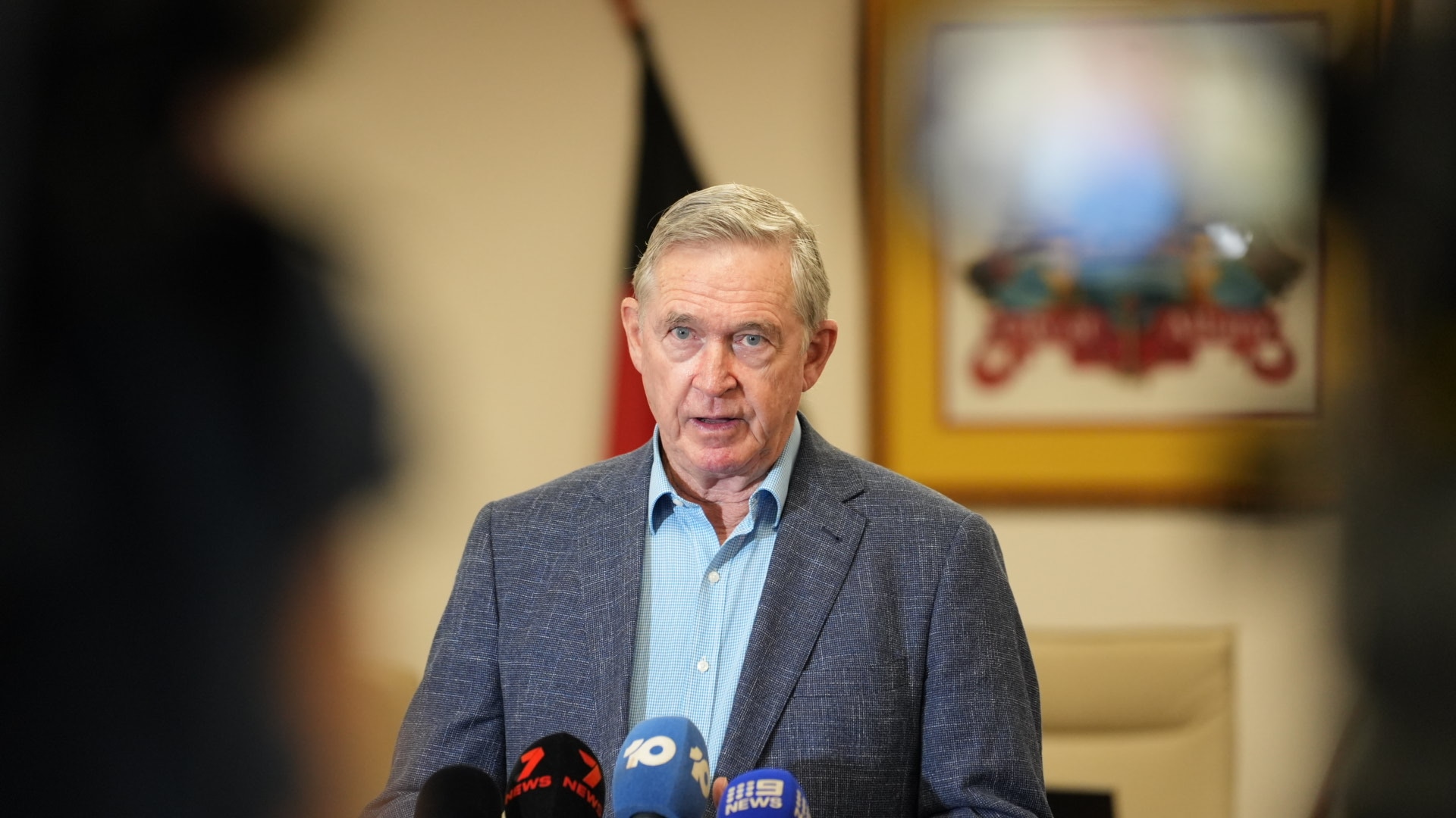 Man wearing suit jacket talking in front of microphones.