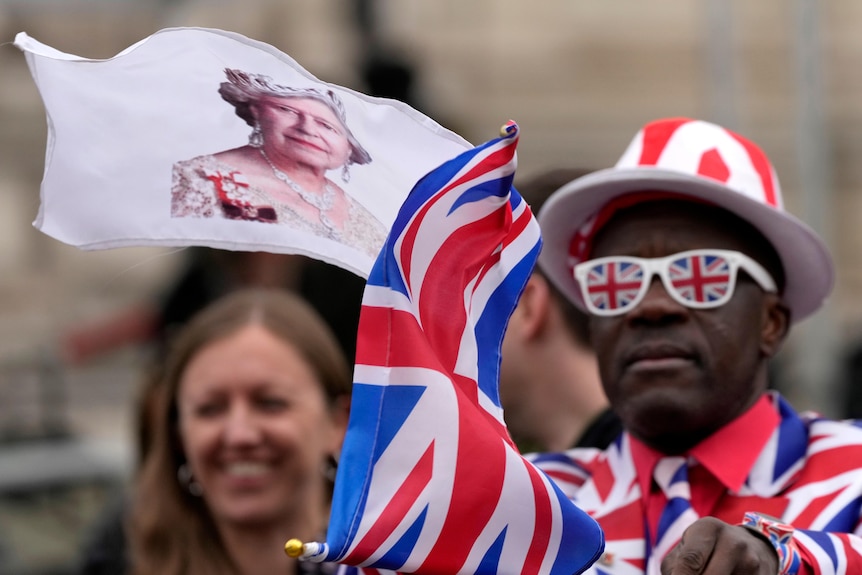 A royal fan waves flags, one with the Queen's face and one a Union Jack, outside Prince Philip's memorial.