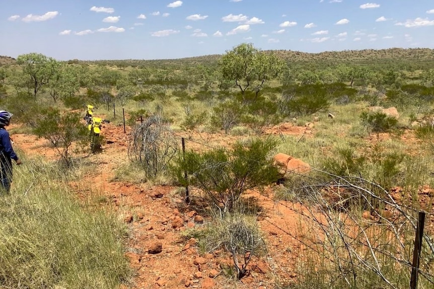 men standing at a wire fence surrounded by red dirt and sparse vegetation