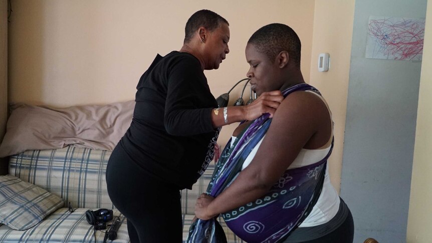 Midwife Claudia Booker helps expectant mother Binahkaye Joy tie a scarf around her shoulders and back.