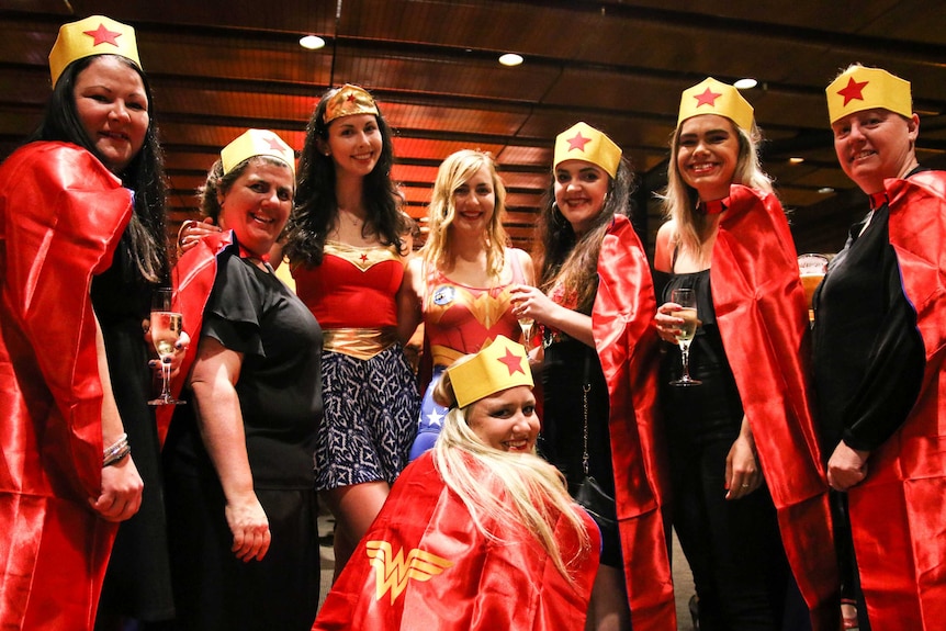 Women dressed up in Wonder Woman costumes stand together holding glasses of champagne