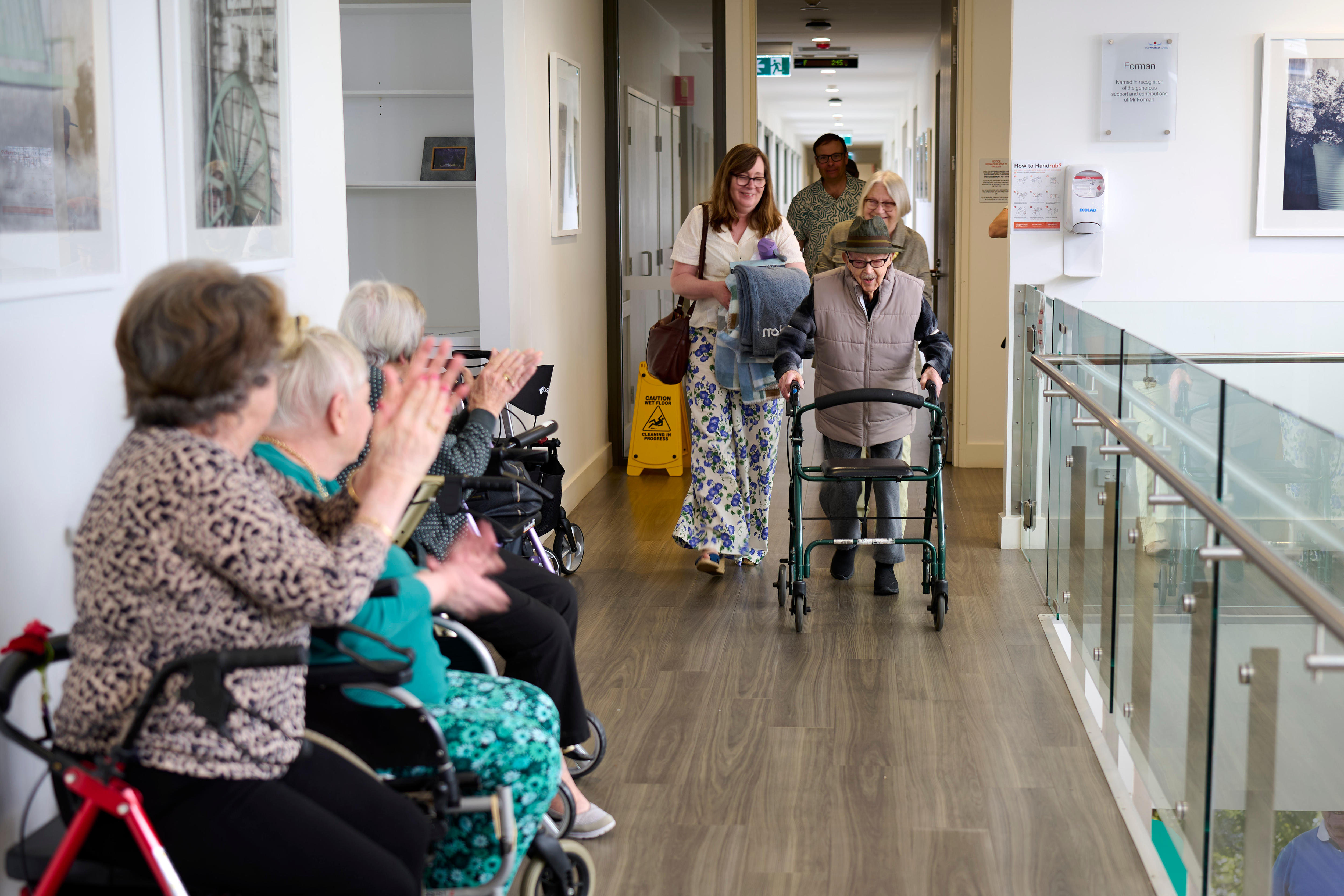 Older people clap as a man with a walker comes towards them.