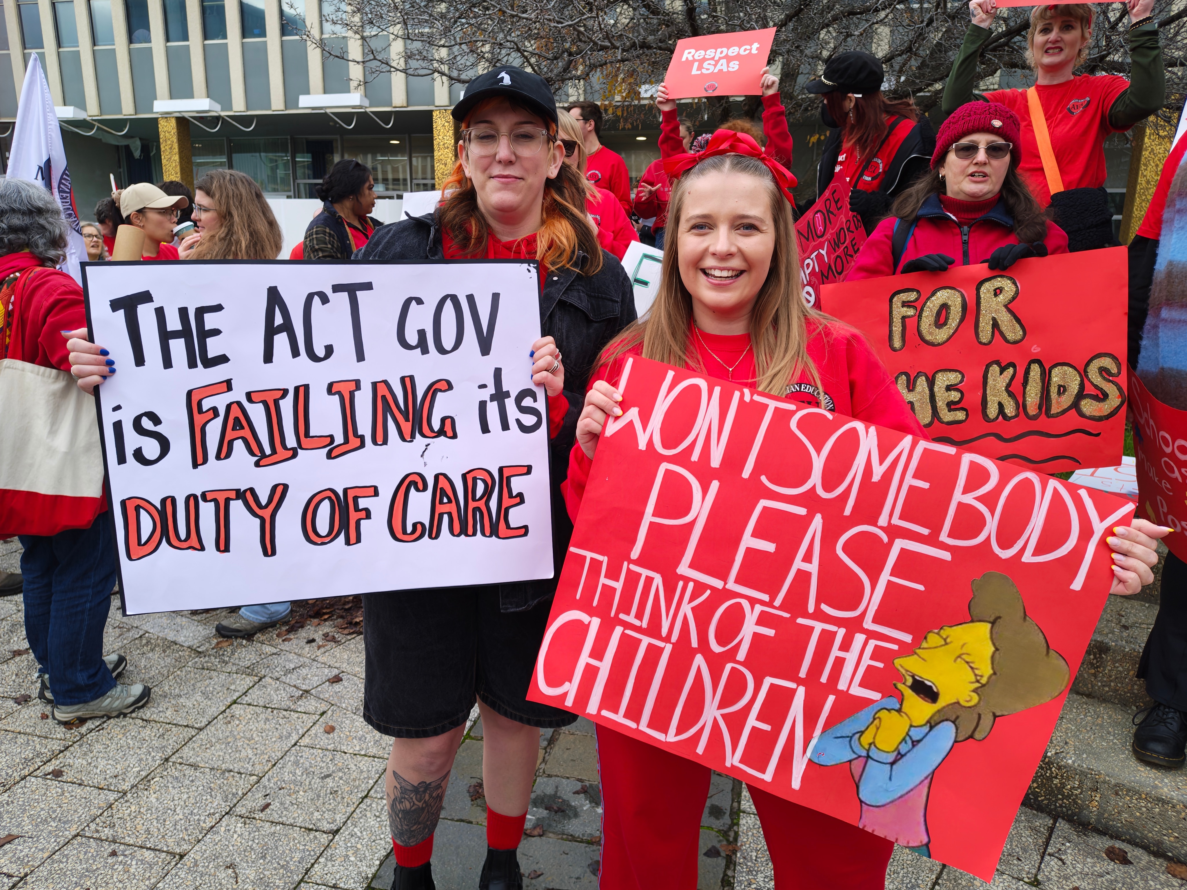People stand wearing red holding protest signs.