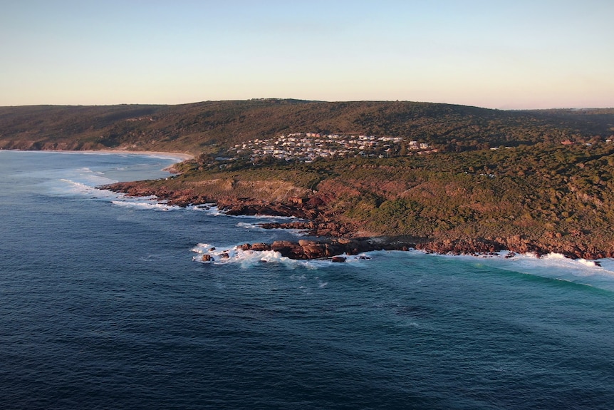 An aerial shot of a town with houses built on a hill overlooking the sea