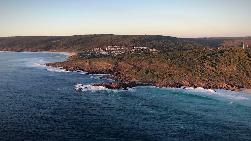 An aerial shot of a town with houses built on a hill overlooking the sea