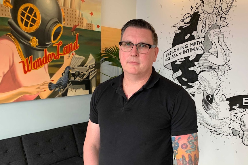 Peter Locke standing in front of two large pieces of art in his office.