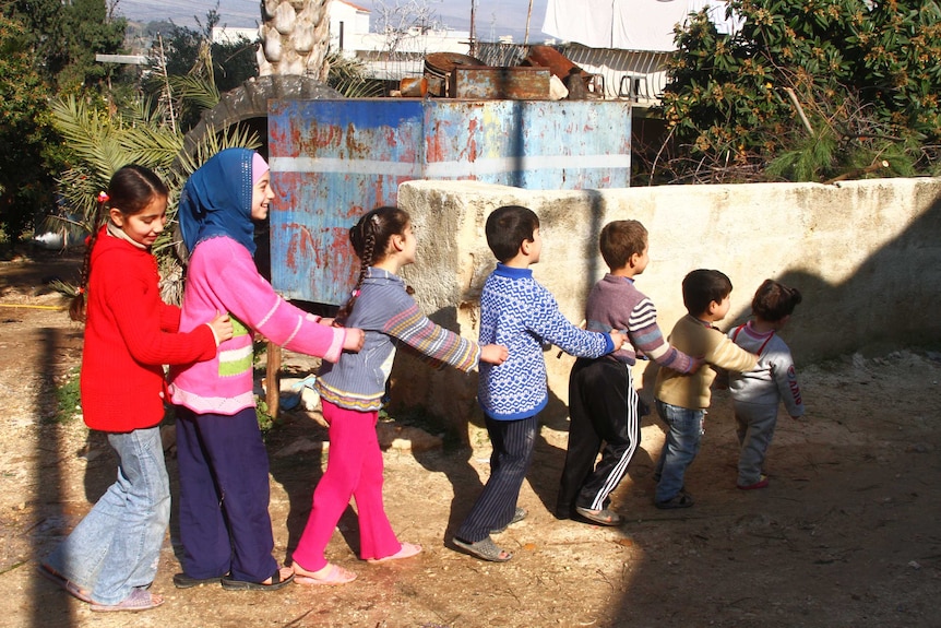 Children walk in a line holding each others waists as they play.