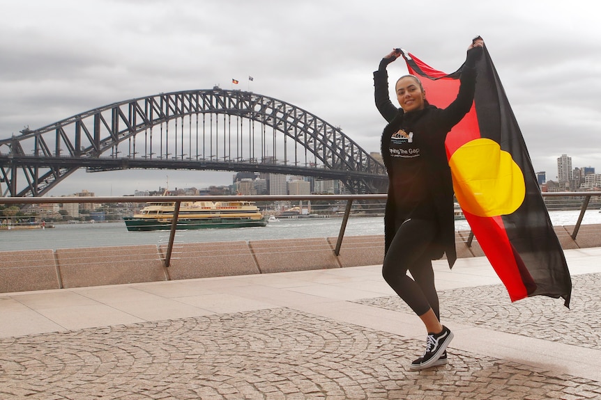 A indigenous woman holding the Aboriginal flag, smiling