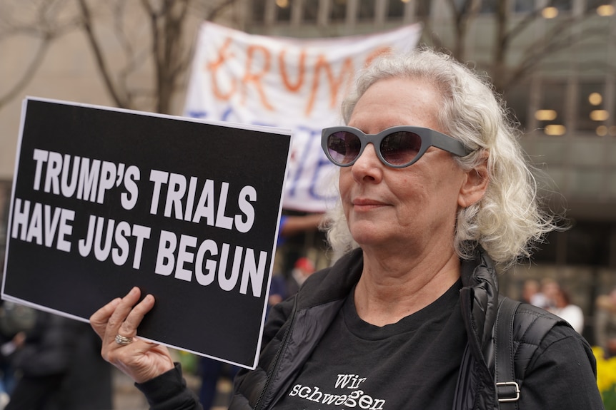 A woman holds a sign about Donald Trump.